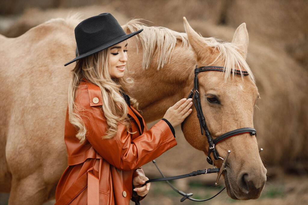 Mujer rubia caballo marron parados granja cerca pacas heno mujer vestido negro abrigo cuero rojo sombrero mujer tocando caballo